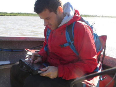 Man in boat wearing red coat looking at rugged tablet