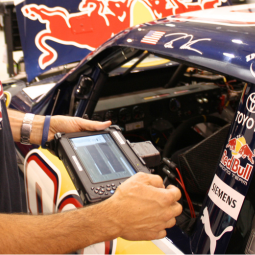 Person holding rugged tablet next to redbull racing car