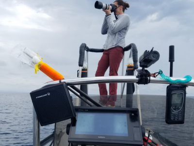 woman standing on boat with large camera in ocean