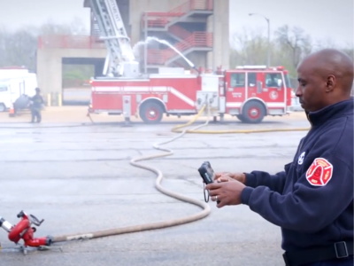 firefighter using rugged tablet to control water pump with firetruck in background