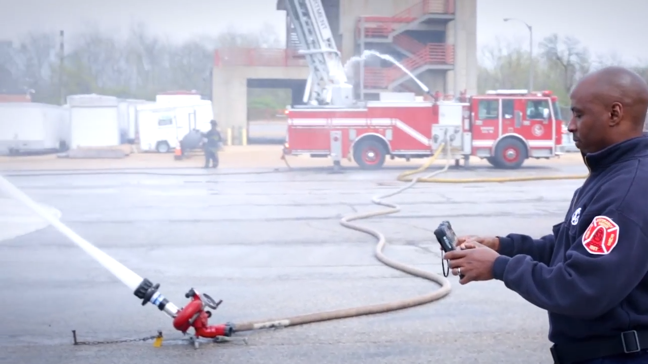 firefighter using tablet to control water hose in front of fire truck