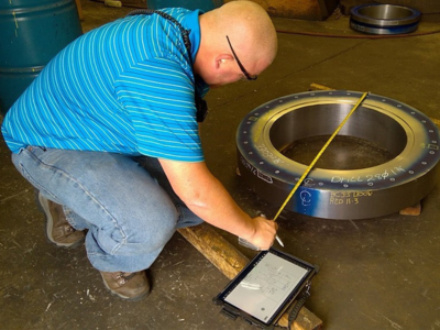 Male employee using tape measure to calculaute diameter of metal tube with rugged tablet