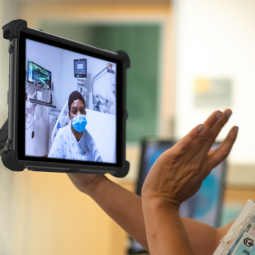 person holding a rugged tablet waving to person on screen