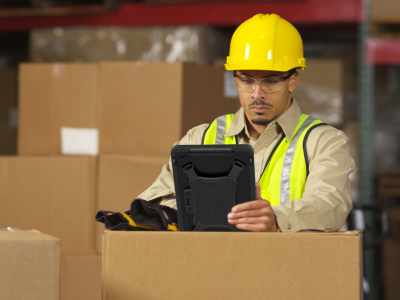 male employee wearing hardhat in warehouse holding rugged tablet